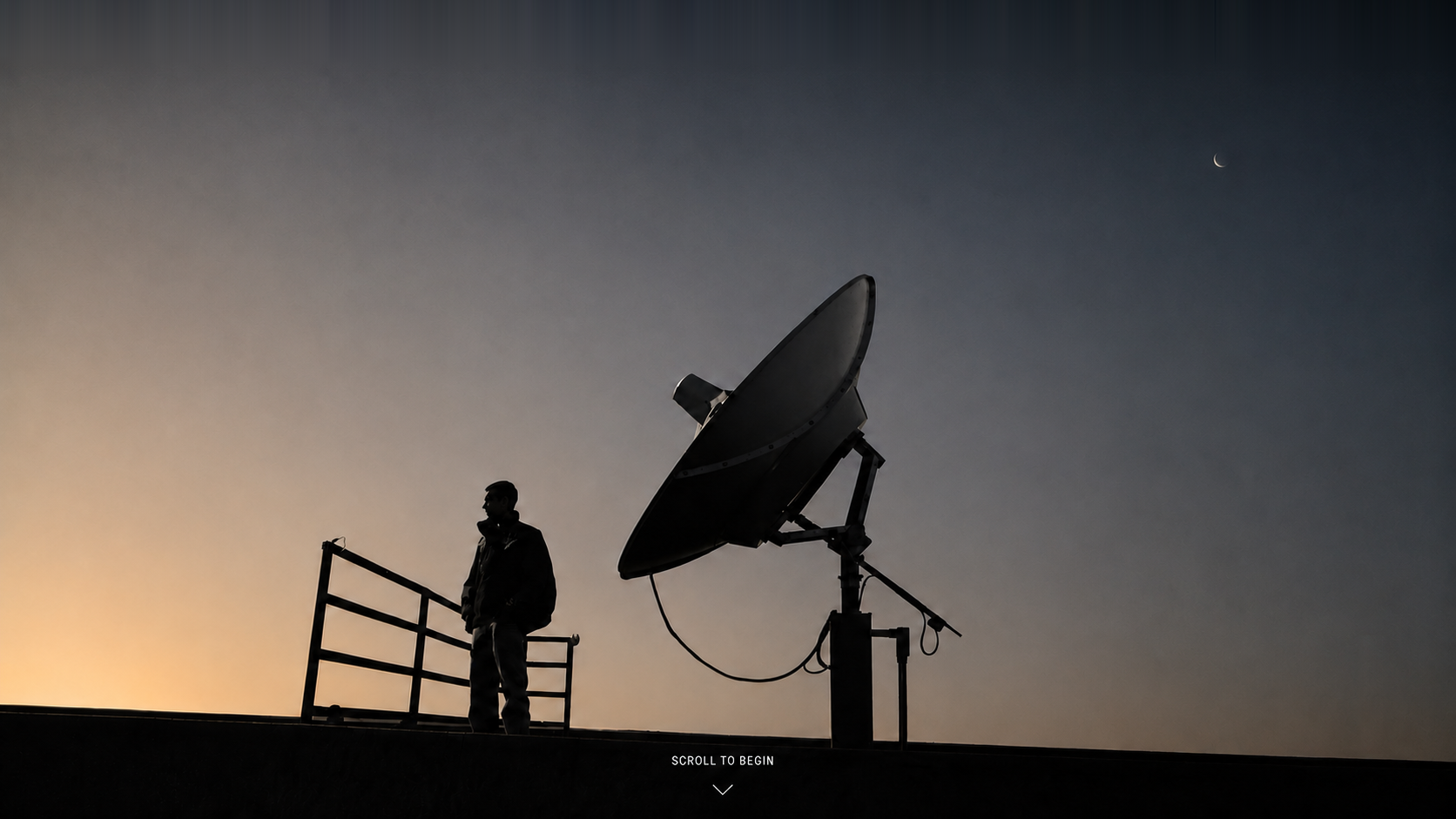 Patrick Duvoisin standing beside a large satellite dish at dusk.
